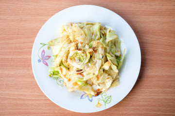 The hot stir fried cabbage with fish sauce serve on white dish set on brown table - homemade food concept.