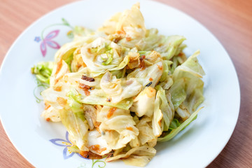 The closeup hot stir fried cabbage with fish sauce serve on white dish set on brown table - homemade food concept.