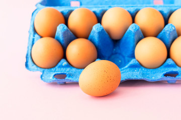 Chicken eggs in blue carton box isolated pink background. Close up