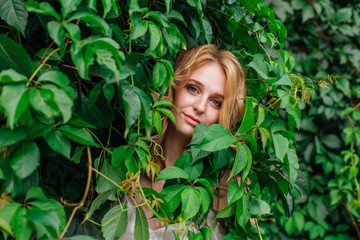 Portrait of a young beautiful woman, hiding in of wild grape leaves.