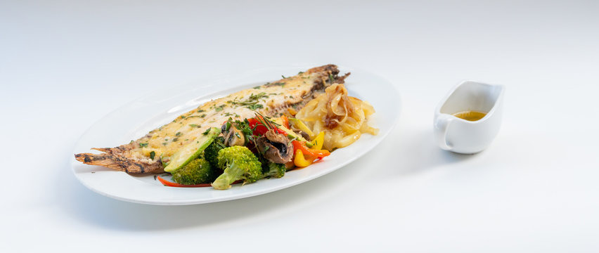 Sole meuni&egrave;re fish with grilled vegetables and caramelized onions on a white plate with white background. LENGUADO MENIER