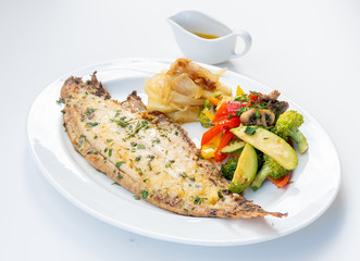 Sole meunière fish with grilled vegetables and caramelized onions on a white plate with white background. LENGUADO MENIER