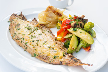 Sole meunière fish with grilled vegetables and caramelized onions on a white plate with white...