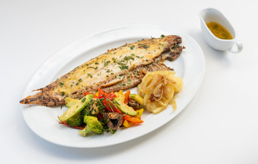 Sole meunière fish with grilled vegetables and caramelized onions on a white plate with white background. LENGUADO MENIER