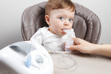 Mother using nebulizer for cute little baby boy sitting on the high chair. Health care concept.