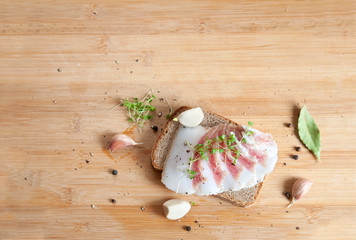 thinly sliced ​​slices of salted lard with streaks of meat lie on bread, mustard sprouts are...