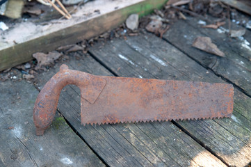Rusty old hand saw lies on a dirty wooden background