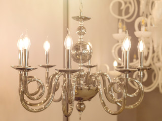 The image of a bright chandelier with metal chrome fixtures and shades in the form of candles. The concept of the classical style in the interior. Close up. Soft warm filter, selective focus.