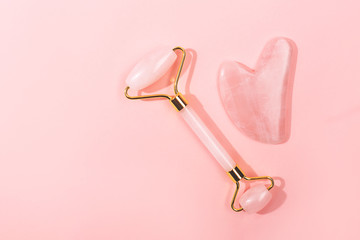 Pink jade roller and gua sha tool on pastel background.