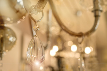A photo of the crystal decor of a drop hanging on the transparent glass armature of the ceiling chandelier in the interior. Concept of luxury design. Close up. Soft warm filter, selective focus.