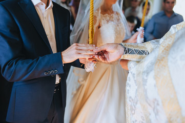 The priest holds a wedding ceremony in the church, rites and puts gold rings on the fingers of the...