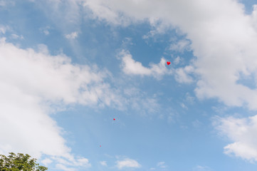 A red heart-shaped balloon flies against a blue sky with clouds. Photography, concept.