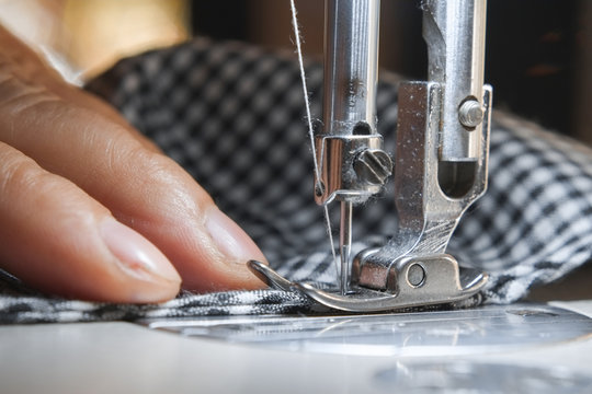 Hand Of Seamstress With Needle Presser Foot And White Thread Of Industrial Sewing Machine To Sew Cloth Close-up.