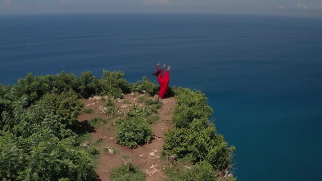 Aerial drone view of happy fit hipster young woman in red dress dance on the cliff mountain. Girl having fun enjoying nature celebrating vacation travel adventure. Adventure lifestyle travel concept.