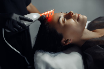 Cosmetologist makes the procedure microcurrent therapy on the hair of a beautiful young woman in cosmetology salon.
