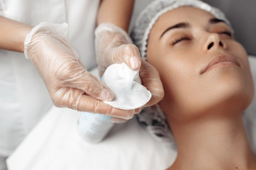 Obraz na płótnie Canvas Cosmetologist applying cream on female face in cosmetology salon.
