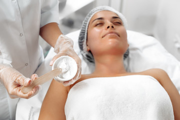 Obraz na płótnie Canvas Cosmetologist applying cream on female face in cosmetology salon.