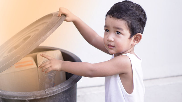 Cute little Asian 2 year old toddler baby boy child throwing plastic bottle in recycling trash bin at public park, Eco friendly kid Recycling, Save the world & environment concept. 
