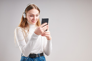 Fototapeta premium Young woman girl listening to music streaming content having fun watching video enjoying video chat talking with friends making gestures faces using smartphone earphones headphones