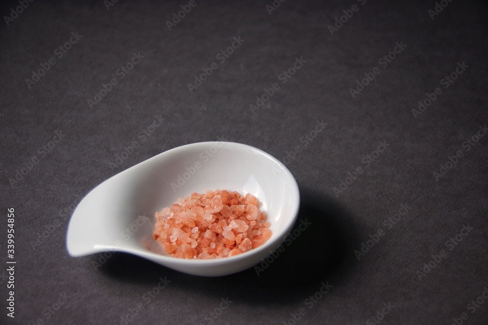 Wall mural closeup of pink himalayan salt in white dish on dark gray background. macro, shallow dof, horizontal