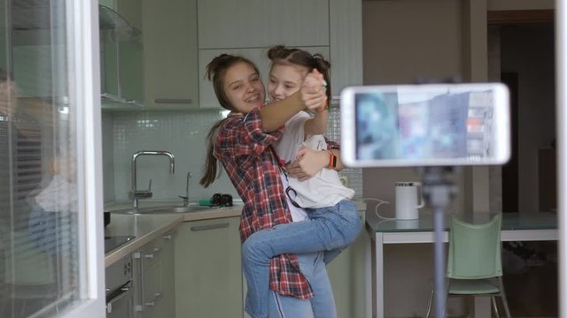 Two sisters dance in the kitchen for a video blog. Girls are vlog shooting themselves on a smartphone in quarantine.