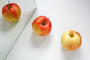 Two apples lie diagonally on a white background, one of them is reflected in the mirror.