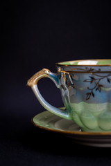 Closeup of half of vintage beautiful coffee cup on vintage plate on dark black background