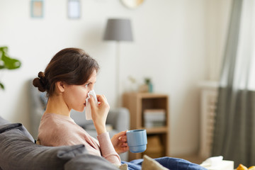 Young woman with her running nose sitting on sofa she caught a flu and sitting at home