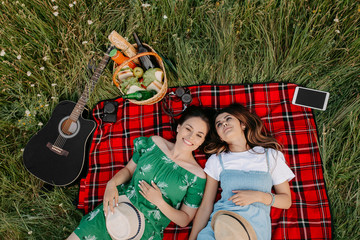 Two cheerful young fashionable women lying down on the picnic blanket and relaxing.