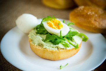 Homemade bun with cheese spread, fresh arugula and boiled egg in a plate