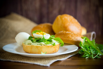 Homemade bun with cheese spread, fresh arugula and boiled egg in a plate