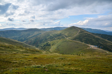 Green fields and mountains, blue sky with clouds. Carpathian mountains in late summer. Hillsides of Svydovets ridge, Carpathians, Ukraine