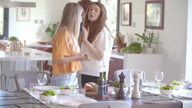 Young woman setting the table in living room putting water carafe for meal while happy friends talking.Happy people group enjoy modern home party dinner or lunch.Handheld video