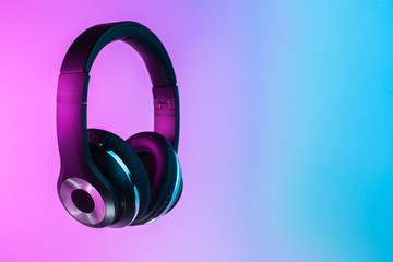 Retro 90s style photo of black stylish wireless headphone in neon lights.