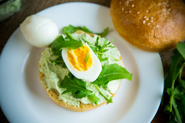 Homemade bun with cheese spread, fresh arugula and boiled egg in a plate
