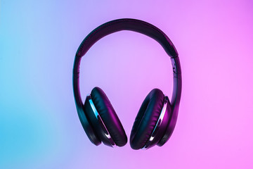 Retro 90s style photo of black stylish wireless headphone in neon lights.