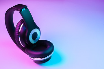 Retro 90s style photo of black stylish wireless headphone in neon lights.