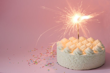 White cream cake on a pink background with a Sparkler. Colorful sprinkles for cakes. Space for text