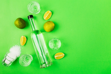 Fototapeta na wymiar Bottle of tequila, lime, salt, shots on green background. Top view, copy space