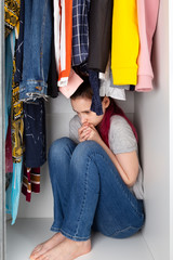Young girl sits in wardrobe clogged into corner. House violence