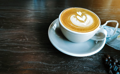 Hot Cappuccino coffee with  protective mask on a wooden table. Concepts of Flu virus, Covid-19 (Coronavirus disease).