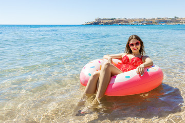 Young girl in red swimsuit is having a rest on doughnut rubber ring in the blue sea. Hot sunny summer concept