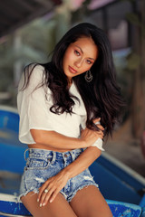 Fototapeta na wymiar lifestyle portrait of young stylish Asian woman seats on blue boat, wearing jeans shorts, smiling enjoy weekends