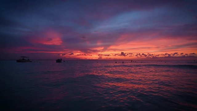 Sunset over the Caraibico Sea of thousands of colors. People in the water and on boats photographing the sunset in Isla Mujeres, Mexico