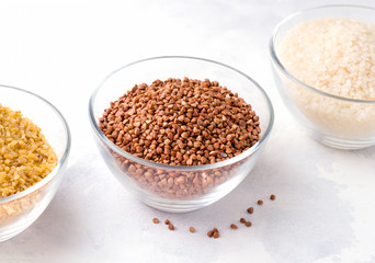 Buckwheat groats and bulgur rice in glass bowls on a concrete background
