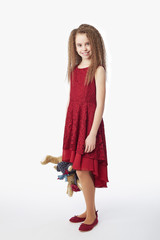 Young girl wearing maroon guipure dress and red flats holding soft toy