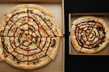 Large and small pizzas lie on an open cardboard box. Black background top view