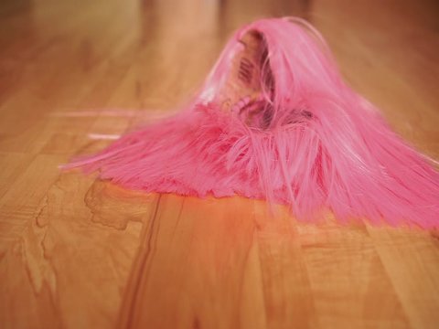 A girl in black shoes walks on a wooden floor and drops a pink wig on the floor. The concept of dressing up, freaks or party