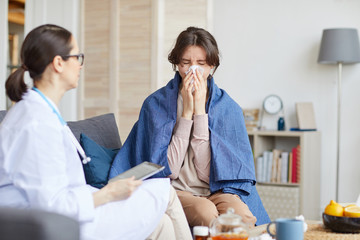 Sick woman has a running nose and talking to female doctor while they sitting on sofa in the living room at home
