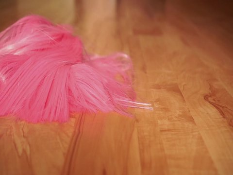 A girl in black shoes walks on a wooden floor and drops a pink wig on the floor. The concept of dressing up, freaks or party